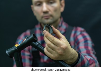 Bicycle Repair. The Bike Mechanic Changes The Cups And Bearings In The Headset Of The Frame. Bicycle Parts In The Workshop On A Black Background. The Face Of A Young Guy With A Tool In His Hands.