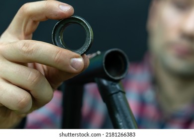 Bicycle Repair. The Bike Mechanic Changes The Cups And Bearings In The Headset Of The Frame. Bicycle Parts In The Workshop On A Black Background. The Face Of A Young Guy With A Tool In His Hands.