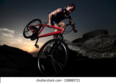 Bicycle Rider Crossing Rocky Terrain At Sunset