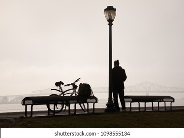 A Bicycle Rider Is Leaning On A Lamp Post In New Orleans With A Bridge Over The Mississippi River In The Background