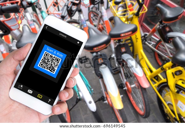 Bicycle sharing\
service or rental technology concept. Sharing economy and\
collaborative consumption. Customer hand using mobile phone to qr\
code application for ride\
bicycle.