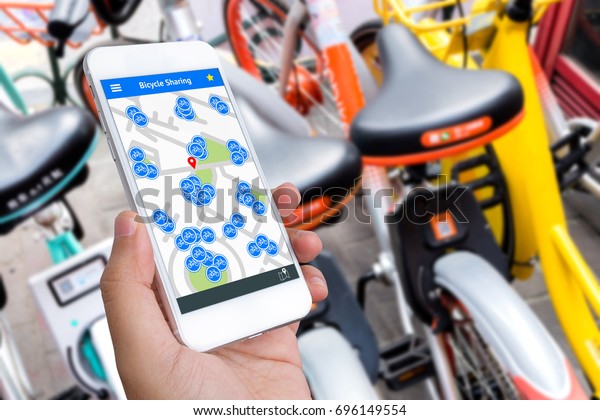 Bicycle sharing service or rental\
technology concept. Sharing economy and collaborative consumption.\
Customer hand using mobile phone to find bicycle for\
ride.