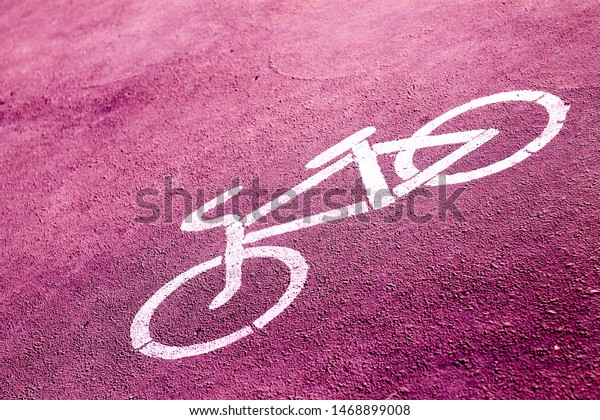bicycle sign\
stencilled with white paint on a bright pink sidewalk indicating a\
designated area for\
cycling