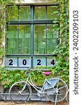 A bicycle standing in front of a window with the number 2024, printed on glass; new year symbolic image 