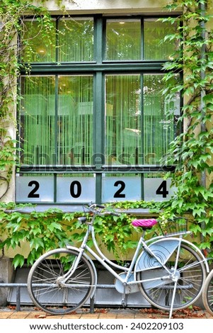 A bicycle standing in front of a window with the number 2024, printed on glass; new year symbolic image 
