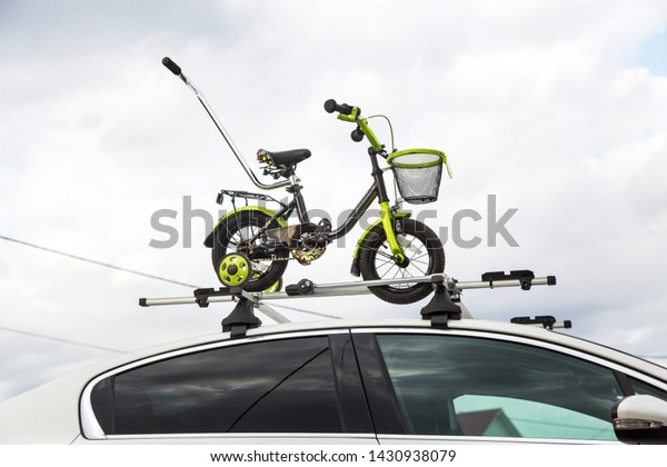Bicycle transportation - a\
children\'s bicycle on the roof of a car against the sky in a\
special mount for cycling. The decision to transport large loads\
and travel by car