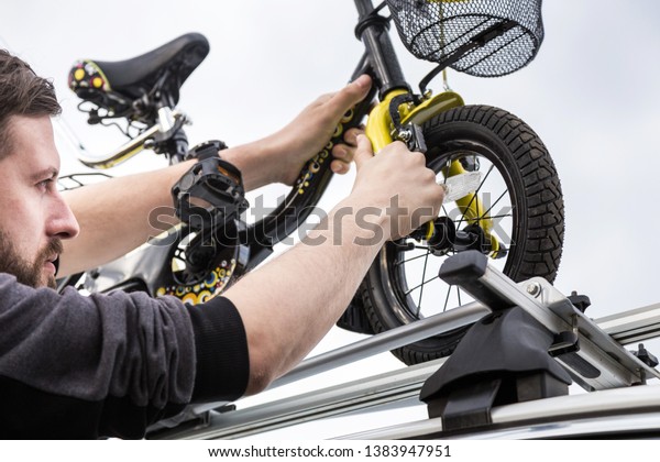 Bicycle transportation - A man fastens and installs
a children's bicycle on the roof of a car in a special mount for
bicycle transport. The decision to transport large loads and travel
by car.