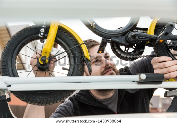 Bicycle transportation - A man fastens and installs\
a children\'s bicycle on the roof of a car in a special mount for\
bicycle transport. The decision to transport large loads and travel\
by car.