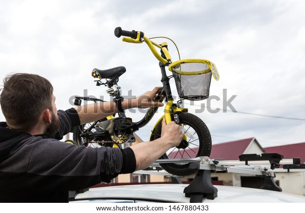 Bicycle transportation - A man fastens and installs\
a children\'s bicycle on the roof of a car in a special mount for\
bicycle transport. The decision to transport large loads and travel\
by car.