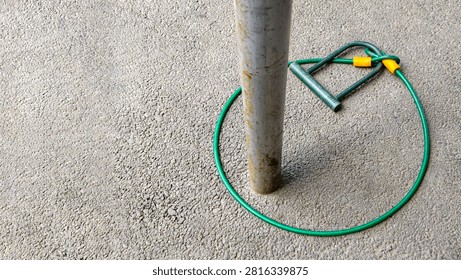Bicycle u lock and cable lock securing itself around a metal pole on asphalt, ironically depicting a concept of failed security, vulnerability, inadequate protection, and misplaced trust