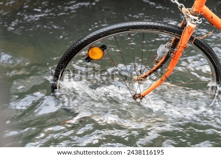 A bicycle is in the water with its tire missing. The water is murky and the bike is in the middle of it