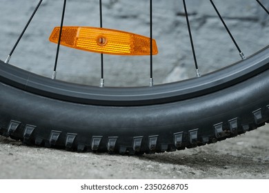 Bicycle wheel with an orange plastic reflector mounted on the spokes. Cycling safety. Outdoors.