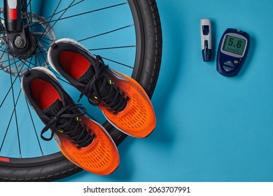 Bicycle Wheel, Orange Sneakers And A Blood Glucose Meter On A Blue Background. Exercise To Normalize Blood Glucose