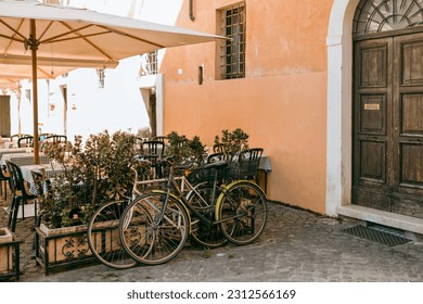 Bicycles parked on the street. Old bike against the orange wall at home. City transport concept. Lush green plants growing in pots near door of house. Cozy old street in Trastevere in Rome, Italy. - Powered by Shutterstock