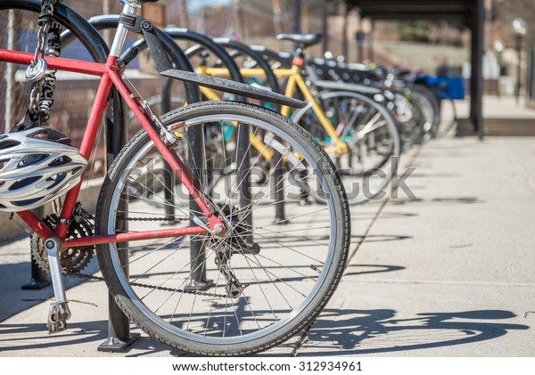 bicycles showing rear wheel  locked and\
parked at the bicycle rack in a row during day\
time