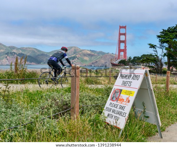Bicyclist passes a warning sign ‘Prevent Auto Theft’\
near the Golden Gate Bridge parking lot - San Francisco,\
California, USA - May 4\
2019