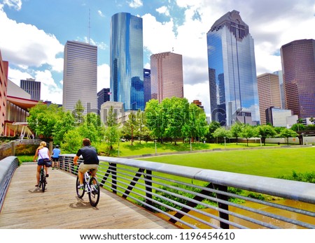 Bicyclists cross wooden bridge in Buffalo Bayou Park, with a beautiful view of downtown Houston (skyline / skyscrapers) in background on a summer day - Houston, Texas, USA 
