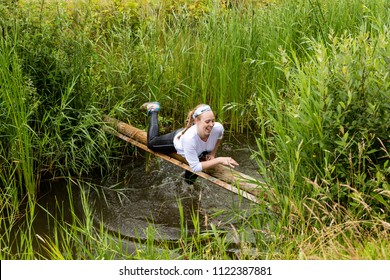 Biddinghuizen, The Netherlands - June 23, 2018: Girl During A Mud Run (mudraise, Charity) In The Mud And In The Water Climbing A Tree Trunk.