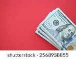 Big amount of hundred dollar bills in thick stack lies on bright red color paper background close up