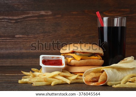Big appetizing hamburger with ketchup and French fries with a coke on the fabric on a brown wooden table