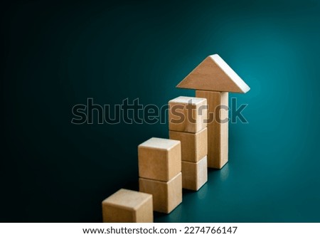 Big arrowhead wooden on increase cube blocks bar graph chart steps on dark blue background with copy space. Investment, income, trends, inflation, business growth, economic improvement concepts.