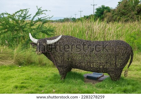 Big artificial buffalo on green yard with long flower grass background at outdoor kid playground.