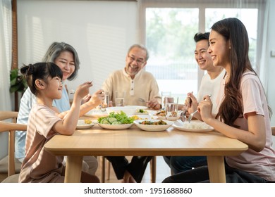 Big Asian happy family spend time having lunch on dinner table together. little kid daughter enjoy eating food with father, mother and grandparents. Multi-Generation relationship and activity in house