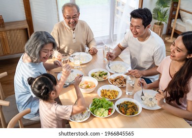 Big Asian happy family spend time having lunch on dinner table together. little kid daughter enjoy eating food with father, mother and grandparents. Multi-Generation relationship and activity in house - Powered by Shutterstock