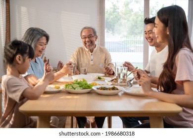 Big Asian Happy Family Spend Time Having Lunch On Dinner Table Together. Little Kid Daughter Enjoy Eating Food With Father, Mother And Grandparents. Multi-Generation Relationship And Activity In House