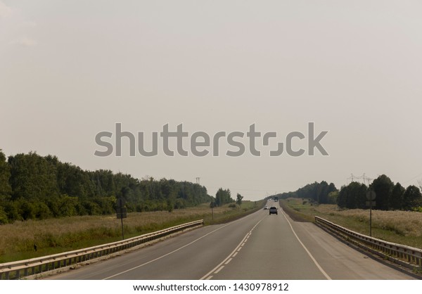 Big autumn field with trees far\
away and clouds in the blue sky. Asphalt road.\
Travelling