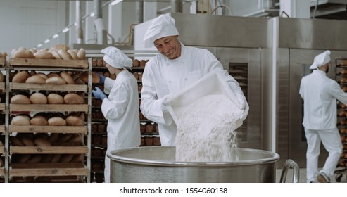 Big bakery industry baker prepare the dough add the flour in a big container background workers arrange the bread and transported the baked bread. - Powered by Shutterstock