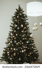 Big beautiful christmas tree decorated with beautiful shiny baubles and many different presents on wooden floor. White wall background with copy space. - Shutterstock ID 2366472829