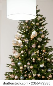 Big beautiful christmas tree decorated with beautiful shiny baubles and many different presents on wooden floor. White wall background with copy space. - Shutterstock ID 2366472835