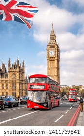 Big Ben with red buses on the bridge against flag of England in London, England, UK