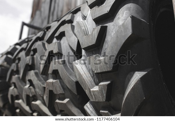 Big black huge big truck, tractor or bulldozer loader\
tires wheel close-up on stand, shop selling tyres for farming and\
big vehicles. Lot of pattern tread of Off-road tires. Construction\
machinery . 