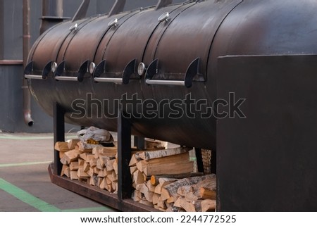 Big black outdoor commercial grill with firewood at summer local food festival. Barbecue, gastronomy, cookery and street food concept