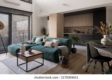 Big, blue and cozy corner sofa in modern living room with big windows open to dark kitchen - Shutterstock ID 2170304651