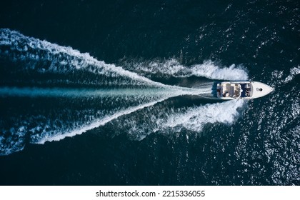 Big Boat In Motion On The Water Top View. Luxury Yacht With People Moving Fast On Dark Blue Water Making A White Trail Behind The Boat, Aerial View.