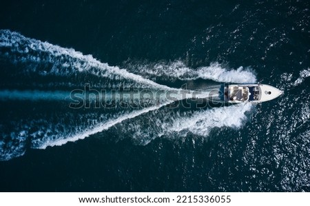 Big boat in motion on the water top view. Luxury yacht with people moving fast on dark blue water making a white trail behind the boat, aerial view.
