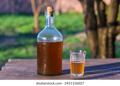Big bottle with a drink made from fermented birch sap on the wooden table on a warm spring day, close up. Traditional Ukrainian cold barley drink kvass in a glass jar and glass in yard
