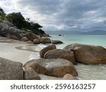 Big boulders in the late afternoon sun. Brown and orange stones, green turquoise sea, sky full of gray and white clouds, mountains in the horizon, green vegetation, sand. Jurere Internacional beach.