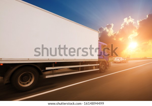 A\
big box truck with space for text and family car driving fast on\
the countryside road against a night sky with\
sunset