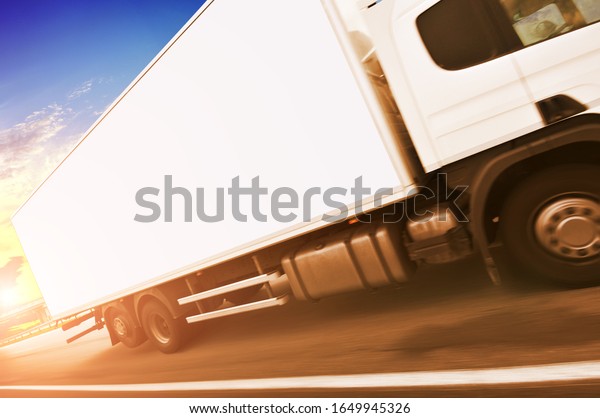 A big box truck with\
space for text on the countryside road in motion against a night\
sky with a sunset