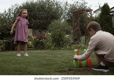 Big brother and little sister play toy bowling with colorful plastic pins and ball on grass in garden or yard or park in summer day - Powered by Shutterstock