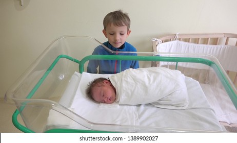 Big Brother Looking To His Newborn Brother, Baby Sleeping In A Bed In Hospital