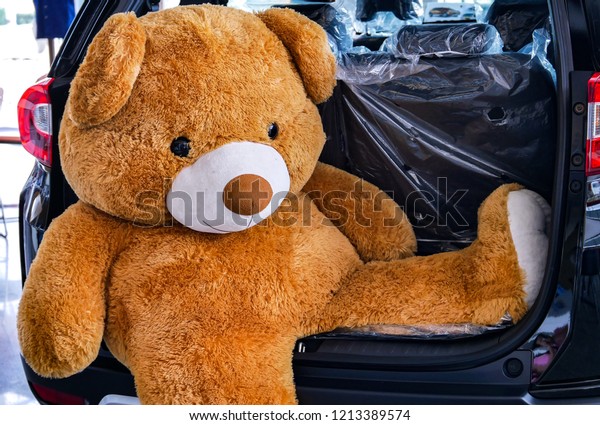 A big\
brown teddy bear doll sitting at the car hood.\
