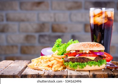 Big burger in classic american style with hot grilled patty with melted cheese on top, tomato, onion, sauces and french fries with cold soft drink served on wooden table. - Powered by Shutterstock