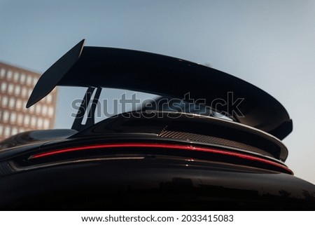 Big carbon spoiler wing on the trunk of a modern supercar. Huge aero kit wing. Sports car coupe tail with big aerodynamic spoiler