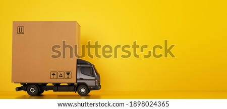 Big cardboard box package on a grey truck ready to be delivered on yellow background