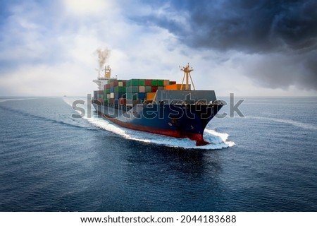 A big cargo container ship travels over calm see with cloudy sky